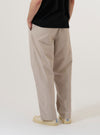 A model wears the Brown Kennedy Stripe Duke Pant, shown from the rear three-quarter angle against a plain white background. The trousers feature a loose, wide-leg fit with a brown and cream vertical stripe pattern. Visible details include two rear buttoned patch pockets and a straight hem. The model is wearing the pants with black shoes.