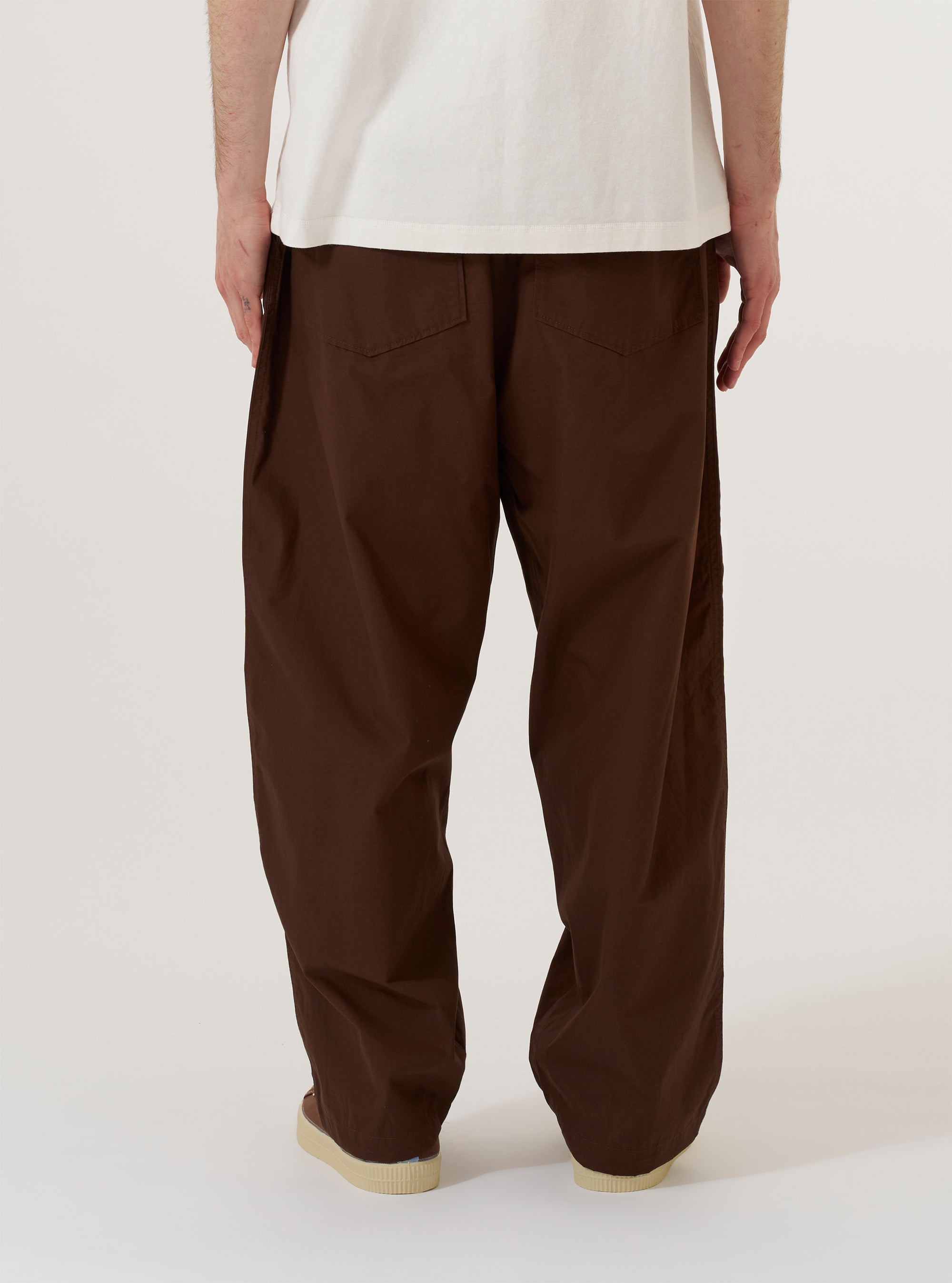 A model is wearing the Brown Peached Poplin Dutch Pant, shown from the waist down against a plain white background. The trousers feature a wide-leg, loose fit and are paired with dark-colored shoes. The peached poplin fabric has a smooth, matte finish.