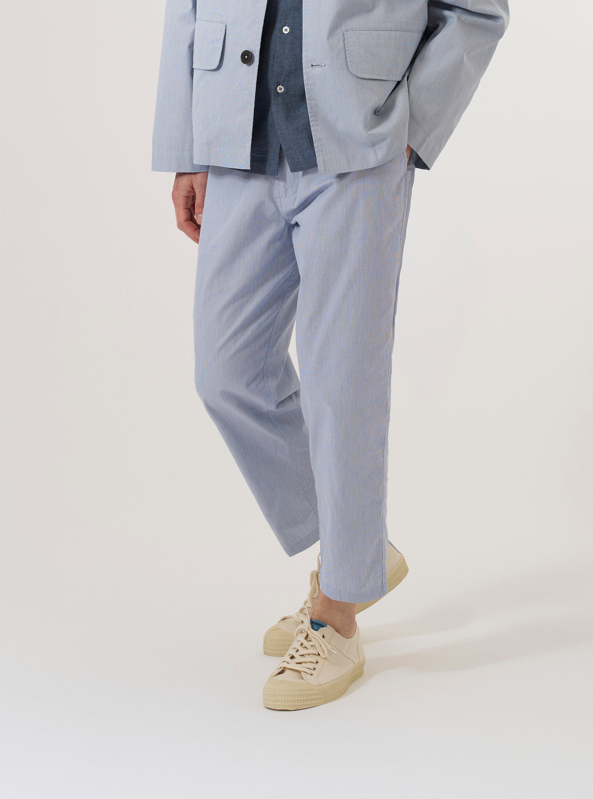 A model wears the Navy Kennedy Stripe Hi Water Trouser, shown from the waist down against a plain white background. The trousers feature a slim, cropped fit with a distinct vertical white stripe pattern on a navy base. The model is wearing them with white socks and dark shoes, highlighting the shortened length and straight hem of the garment.