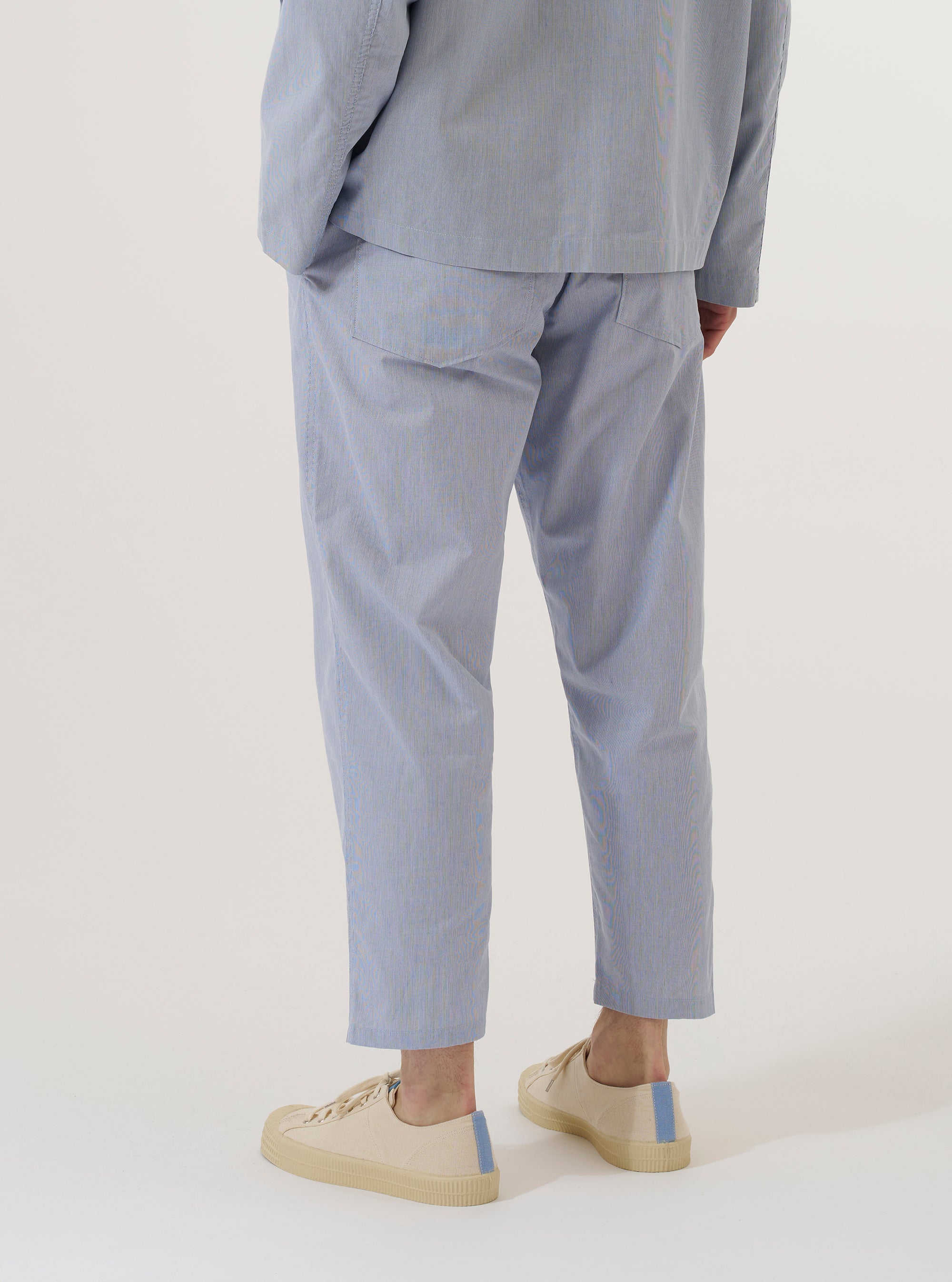 A model wears the Navy Kennedy Stripe Hi Water Trouser, shown from a rear three-quarter angle against a plain white background. The trousers feature a slim, cropped fit and a vertical stripe pattern throughout. The garment includes a drawstring waistband and a single rear patch pocket on the right side.