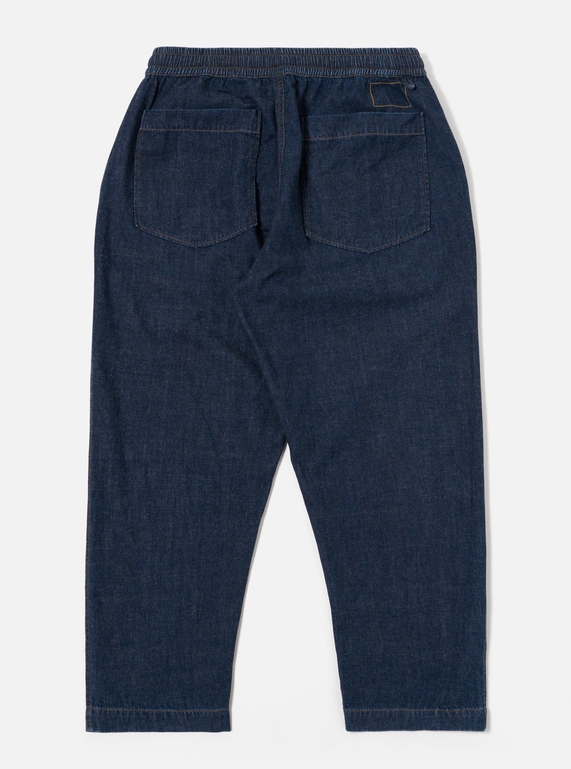 The Indigo Kaihara LT WT Denim Hi Water Trouser is shown from a rear angle as a flat lay against a plain white background. The trousers feature an elasticated waistband and two large rear patch pockets. The lightweight indigo denim fabric shows visible stitching details around the pockets and seams.