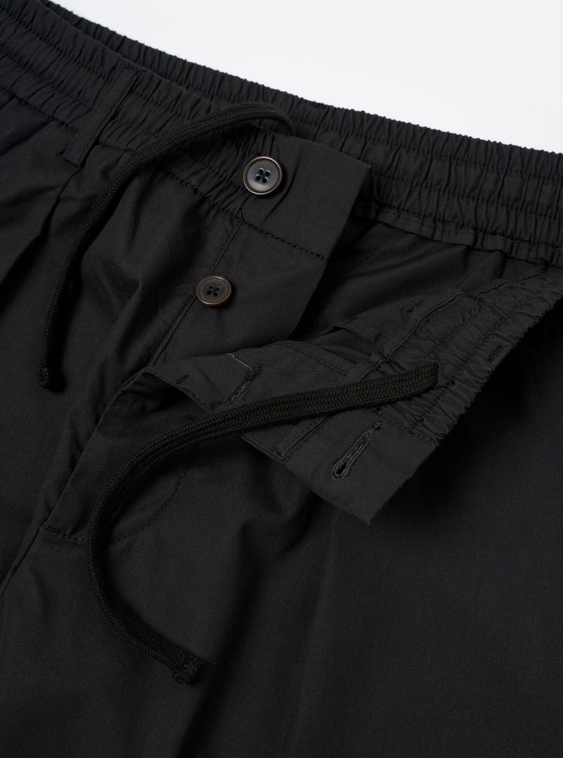 The Black Recycled Polytech Pleated Track Pant is shown from a rear three-quarter angle as a flat lay against a plain white background. The image highlights the tapered leg, a rear patch pocket with a buttoned flap, and the smooth, technical texture of the black recycled polytech fabric.