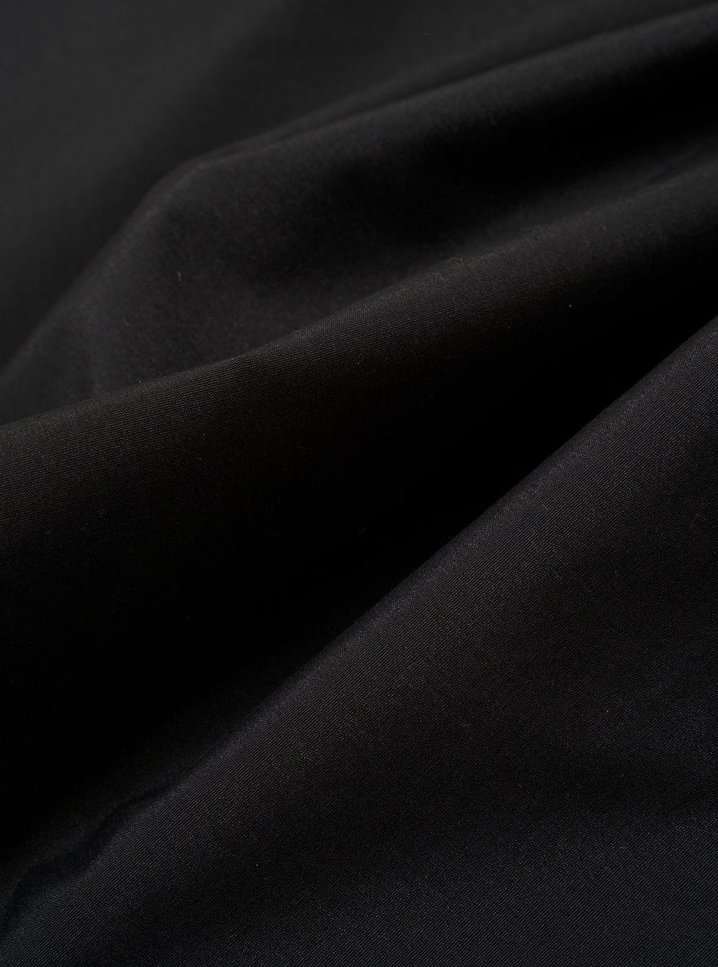 The Black Recycled Polytech Pleated Track Pant is shown in a close-up detail shot against a plain white background. The image focuses on the rear of the garment, highlighting the clean construction of the elasticated waistband and a single rear patch pocket. The black recycled polytech fabric has a smooth, technical finish with visible tonal stitching.
