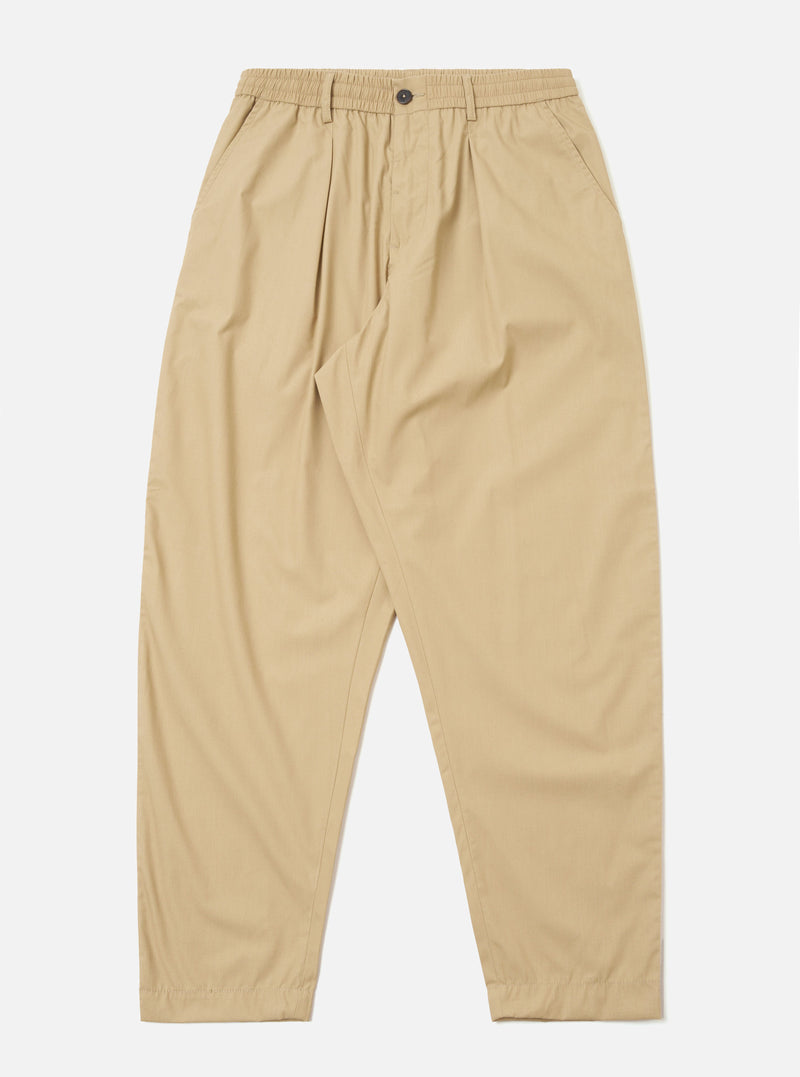 The Sand Recycled Polytech Pleated Track Pant is displayed as a flat lay against a plain white background. The trousers feature an elasticated waistband with an internal drawstring, a single pleat at the front of each leg, and a tapered silhouette. Two side pockets are visible. The fabric is a smooth, sand-colored recycled polytech material.