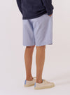 The Navy Kennedy Stripe Pleated Track Short is shown from a rear three-quarter angle as a flat lay against a plain white background. The shorts feature a vertical white pinstripe pattern on a navy blue base, an elasticated waistband, and a single rear patch pocket on the right side. The fabric appears to be a structured cotton.
