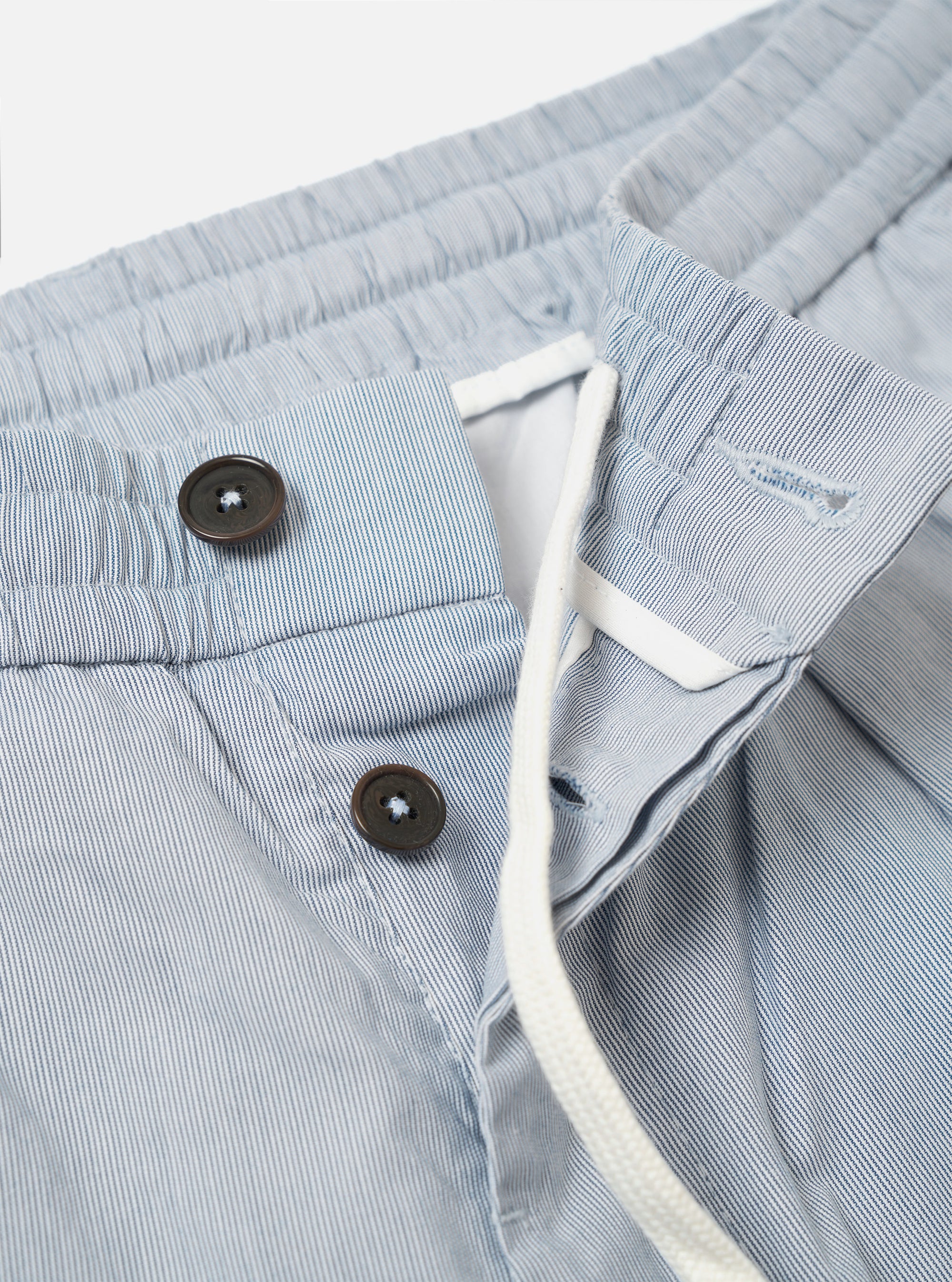 The Navy Kennedy Stripe Pleated Track Short is shown from a rear angle as a flat lay against a plain white background. The shorts feature a single patch pocket on the right side and an elasticated waistband. The fabric is a navy blue cotton with thin, vertical white stripes.