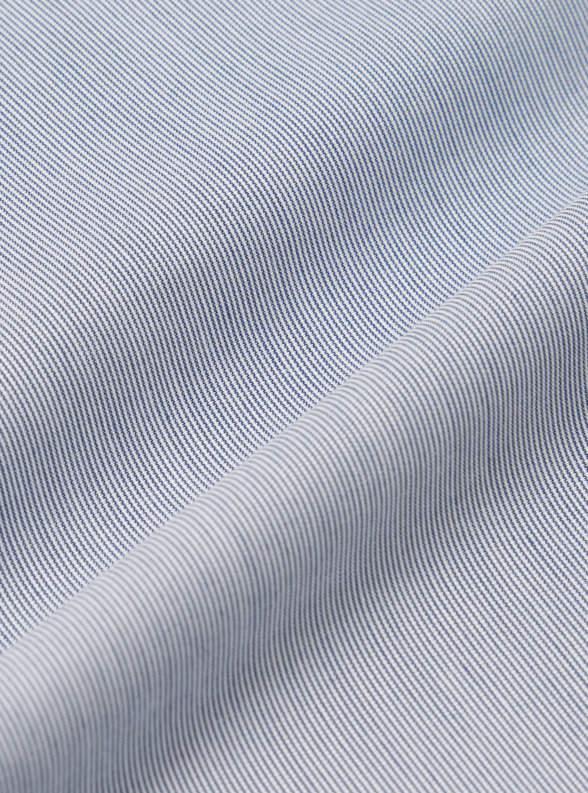 A close-up fabric swatch of the Navy Kennedy Stripe Pleated Track Short highlights the texture and pattern of the material. The navy blue fabric features a distinct vertical stripe design. The material fills the entire frame, providing a detailed view of the garment's color and construction.