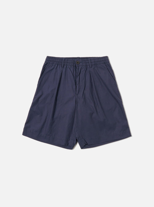 The Navy Peached Poplin Pleated Track Short is shown as a flat lay against a white background. The shorts feature a single pleat on the front, an elasticated waistband with a button closure, and two side hand pockets. The navy cotton fabric has a smooth, peached finish.