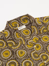 The Olive Cape Block Print Camp Shirt is shown in a detail view as a flat lay against a plain white background. The image highlights the side split hem, which is slightly longer at the back, and the loose fit of the short sleeve. The hand-printed olive pattern is clearly visible on the cotton fabric.