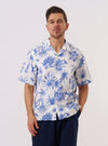 A model wears the White Jungle Toile Poplin Camp Shirt against a plain white background. The shirt features an all-over dark jungle toile print on a white base, a relaxed camp collar, and a central button-down front. The model is shown from the chest up with the shirt worn open over a white T-shirt.