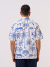 The White Jungle Toile Poplin Camp Shirt is worn by a model against a plain, light grey background. This rear three-quarter view highlights the shirt's relaxed fit and the intricate dark jungle toile pattern featuring animals and tropical foliage against a white base. The model wears the short-sleeved shirt untucked, showcasing the straight hem and the smooth texture of the cotton poplin fabric.