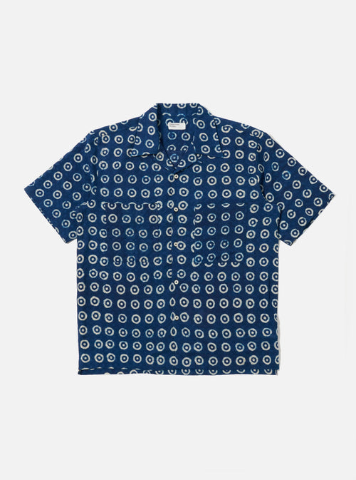 The Indigo Block Print Circles Camper Shirt is shown as a flat lay against a plain white background. The shirt features a relaxed camp collar, a button-down front, and a single chest pocket. The dark indigo cotton fabric is decorated with an all-over white hand-block printed pattern consisting of repetitive concentric circles.