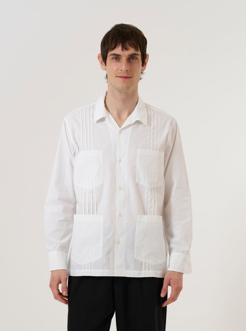 A model wears the White Poplin Dwight Overshirt against a plain white background. The overshirt features a camp collar, a central button-down front, and two large chest pockets with buttoned flaps. The lightweight white cotton poplin fabric has a smooth finish, and the garment is worn as a top layer over a dark T-shirt.