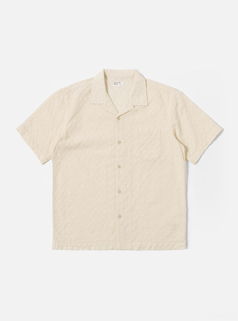 The Ecru Dot Waffle Road Shirt is shown as a flat lay against a white background. The short-sleeve shirt features a camp collar with a loop closure, a central button-down front, and a single patch pocket on the left chest. The ecru-colored cotton fabric has a distinct dot waffle texture and a straight hem.