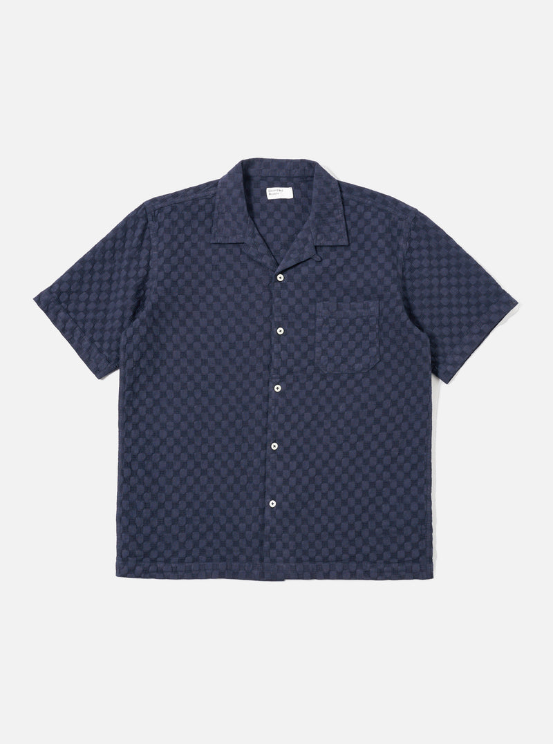 The Navy Dot Waffle Road Shirt is shown as a flat lay against a plain white background. The shirt features short sleeves, a camp collar with a loop closure at the neck, and a single chest patch pocket on the left side. The fabric has a distinct textured waffle pattern throughout.