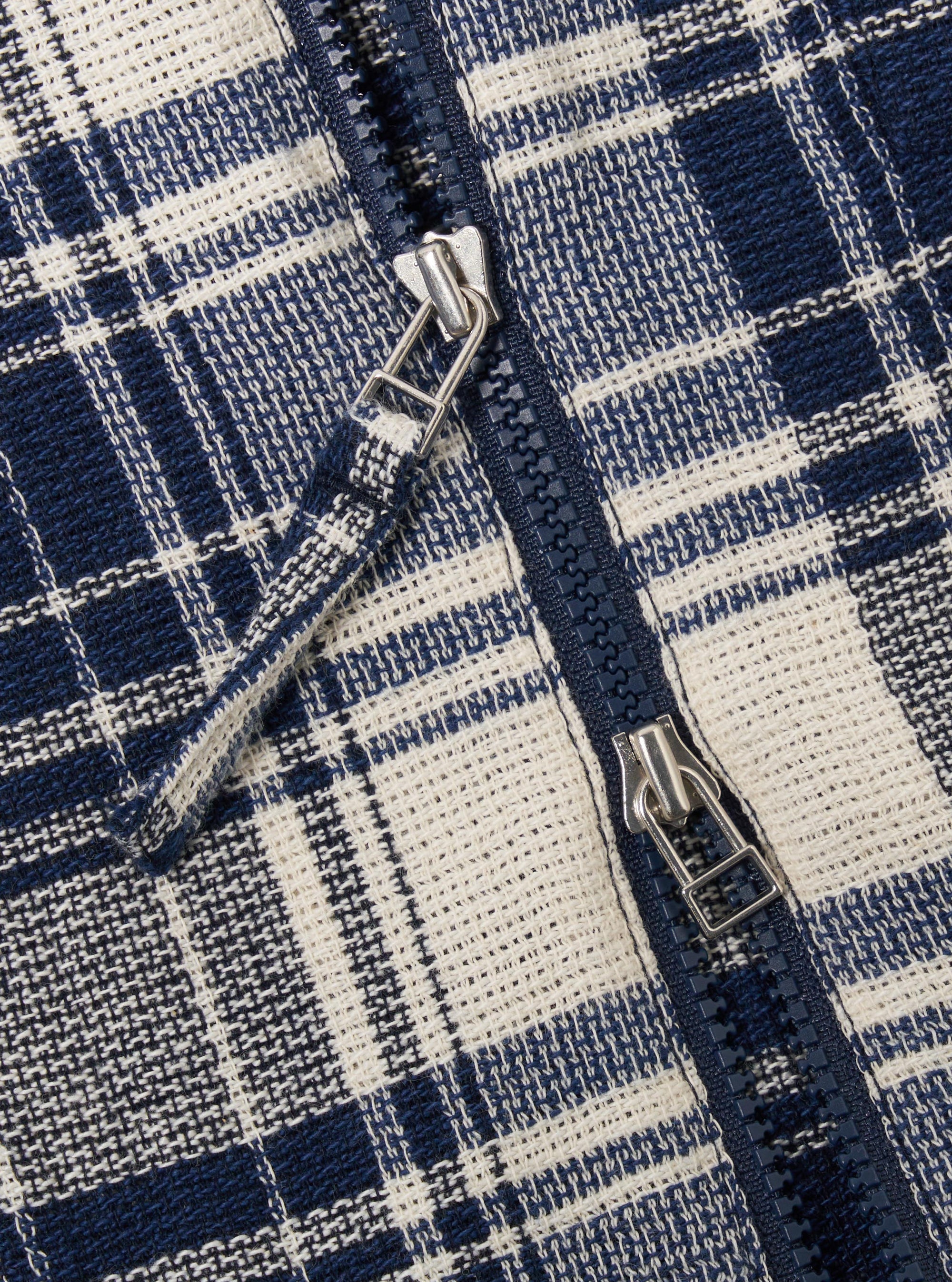 The Navy Texture Plaid Zip Shirt is shown from a rear angle as a flat lay against a plain white background. The image highlights the shirt's relaxed fit, straight hem, and the detailed texture of the navy blue plaid cotton fabric. A simple locker loop is visible at the center of the back yoke.