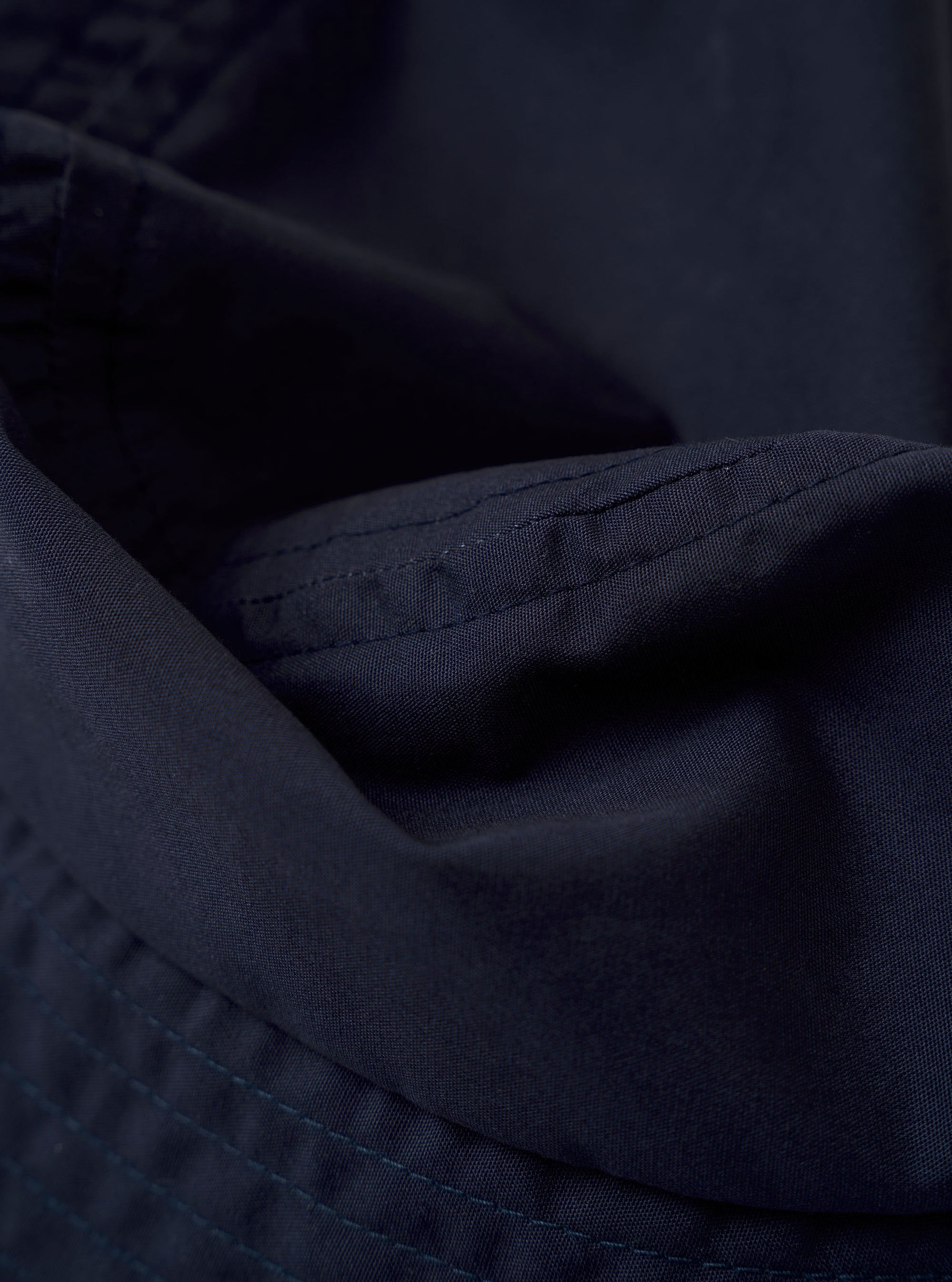 The Navy Recycled Polytech Beach Hat is shown as a flat lay against a plain white background. The hat features a classic bucket-style design with a flat crown and a wide, downward-sloping brim with tonal stitching. The material is a smooth, dark navy recycled polytech fabric with a technical finish.