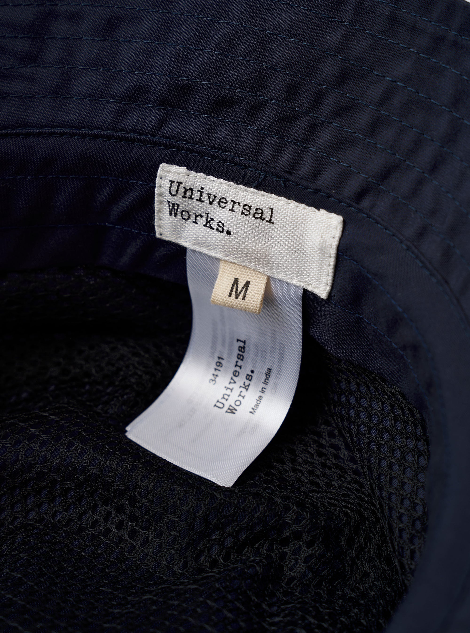 The Navy Recycled Polytech Beach Hat is shown in a detail view as a flat lay against a plain white background. The image highlights the interior of the bucket hat, showing the mesh lining, the brand label, and the internal sweatband. The dark navy fabric and the dual metal ventilation eyelets on the side are also visible.