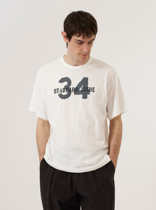 A model wears the Ecru Single Jersey 34 Printed Core Tee against a plain, neutral background. The short-sleeved t-shirt features a crew neckline with a self-bound neck and a graphic print on the chest. The ecru cotton jersey fabric has a soft texture, and the garment is shown in a relaxed, generous fit.