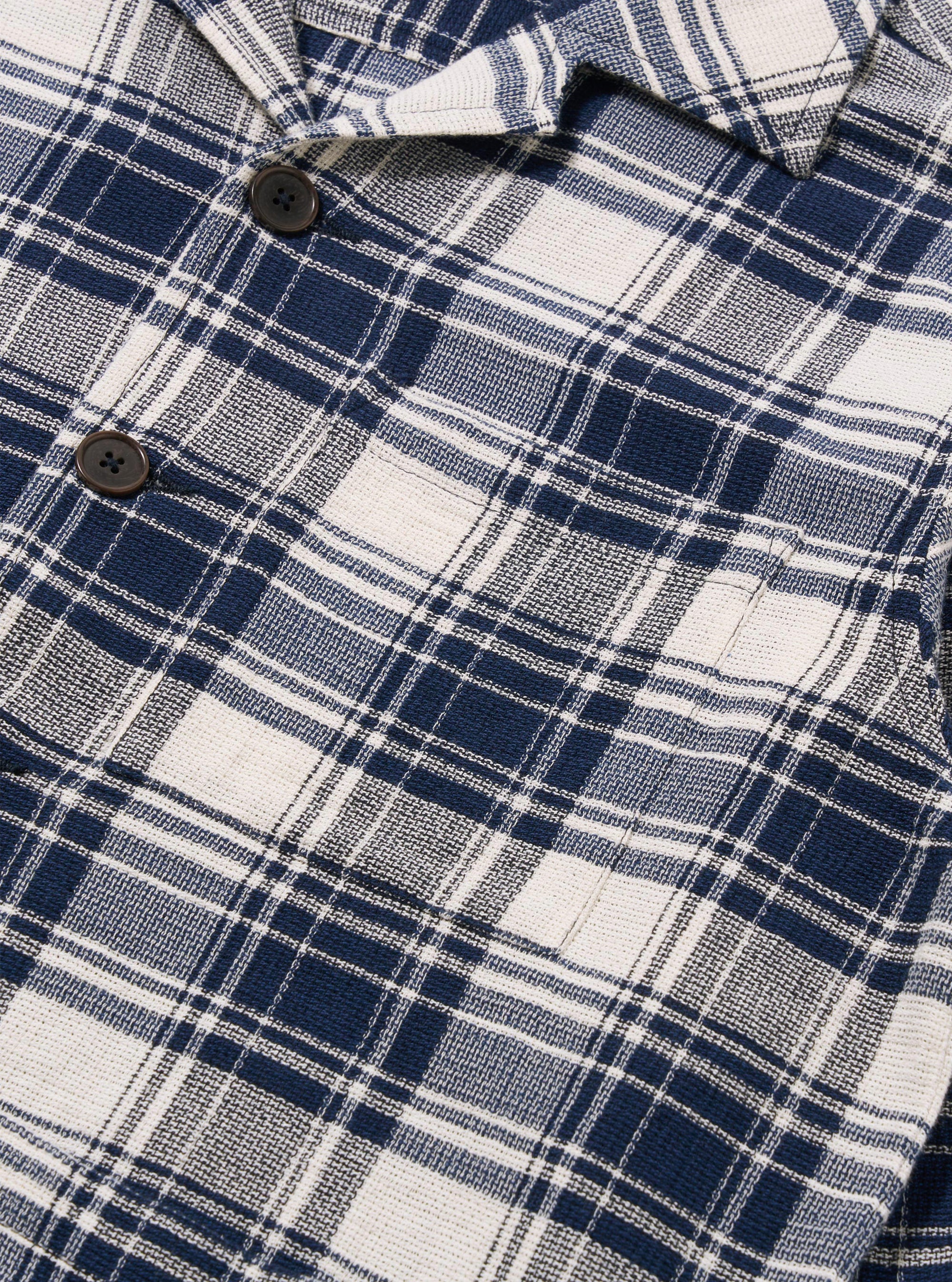 The Navy Texture Plaid Cancun Jacket is shown from the back as a flat lay against a plain white background. The image highlights the jacket's boxy fit, double back vents, and the detailed texture of the navy blue plaid cotton fabric.