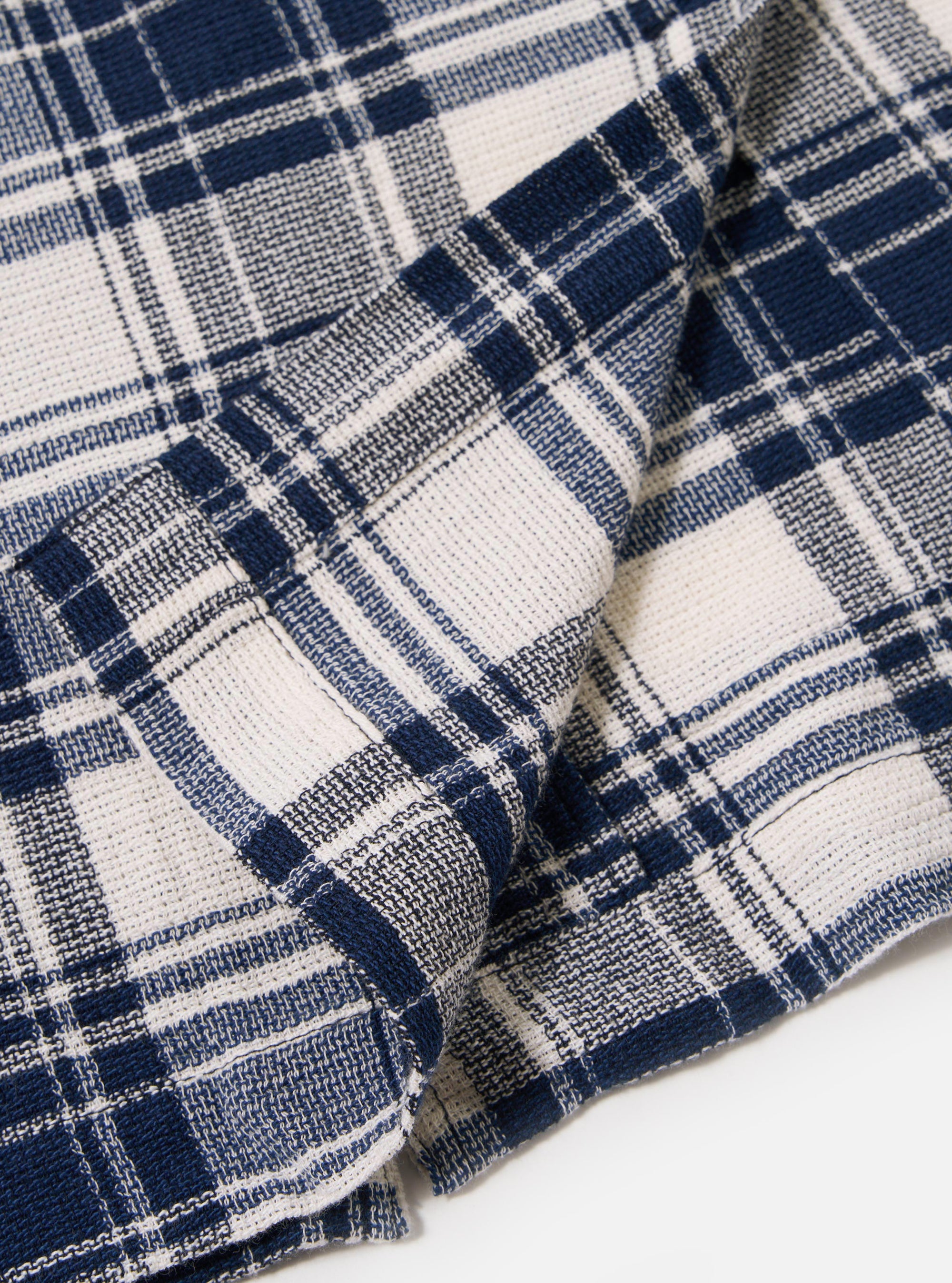 The Navy Texture Plaid Cancun Jacket is displayed as a flat lay against a plain white background. The image provides a close-up detail of the jacket's lower front, highlighting a large patch pocket and the textured navy blue plaid pattern of the cotton fabric.