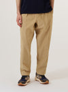 A model wears the Sand Organic Fine Cord Oxford Pant against a plain, neutral background. The trousers feature a wide, loose fit with a single pleat at the front and an elasticated waistband with a visible drawstring. The sand-colored organic cotton fabric has a fine, vertical corduroy texture.