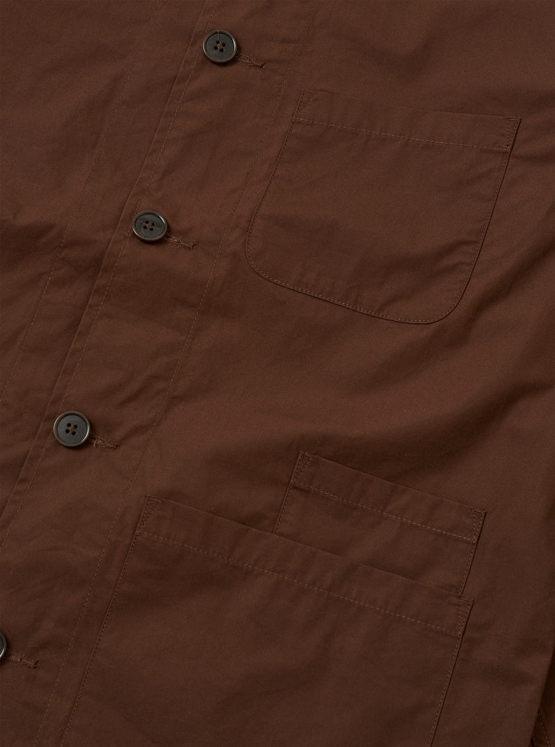 The Brown Peached Poplin Bakers Overshirt is shown from the back as a flat lay against a plain white background. The image highlights the clean construction of the garment's rear panel, featuring a straight hem and a simple, smooth finish on the brown cotton poplin fabric.