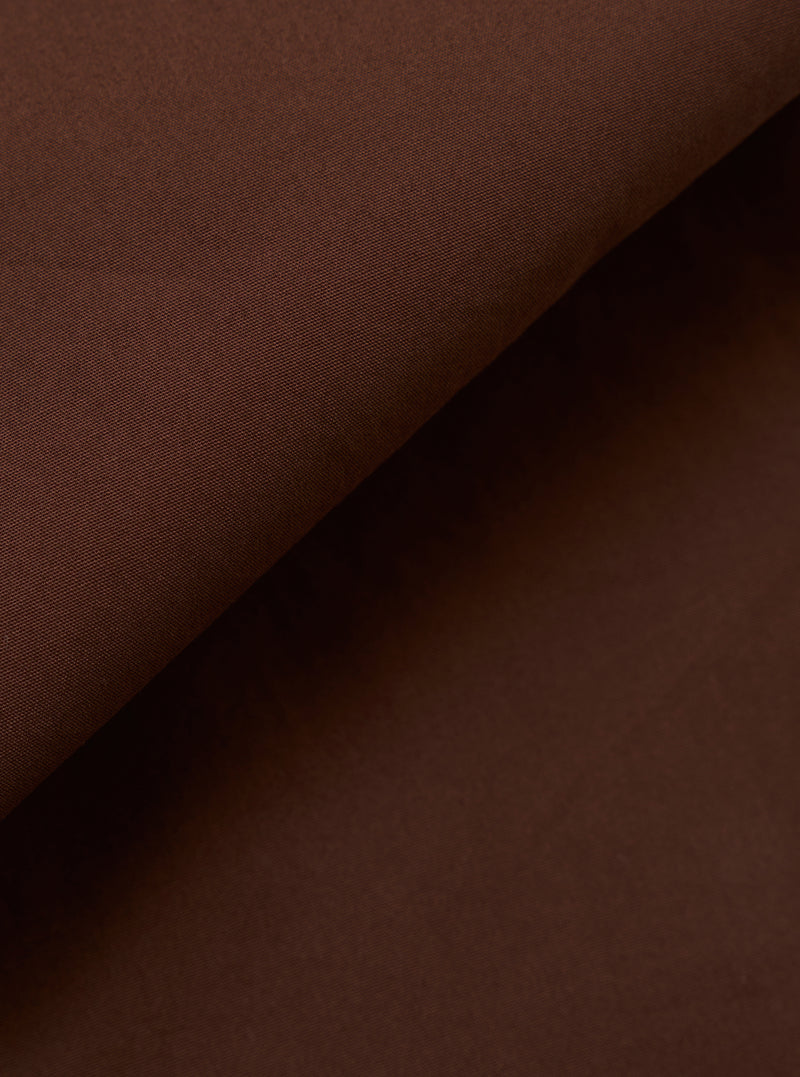 A close-up swatch image of the Brown Peached Poplin Military Chino fabric highlights the solid brown color and the smooth, matte finish of the peached poplin material. The textile's fine weave is clearly visible.