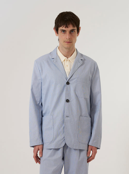 A model wears the Navy Kennedy Stripe Three Button Jacket over a light-colored shirt, standing against a plain white background. The jacket features a three-button front closure, three large patch pockets, and a classic lapel. The fabric has a vertical pinstripe pattern throughout.
