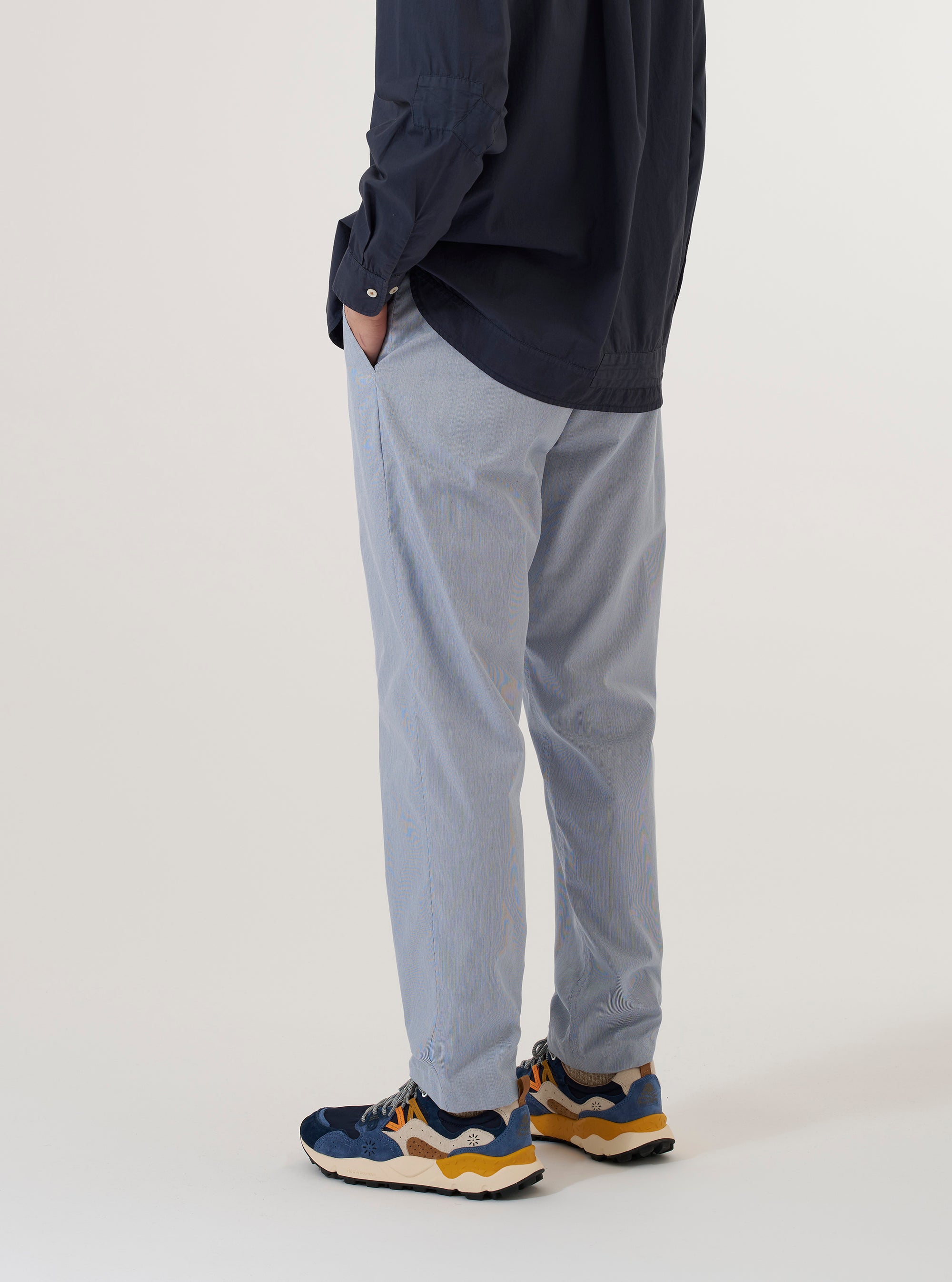 A model wears the Navy Kennedy Stripe Military Chino, shown from the waist down against a plain white background. The trousers feature a vertical navy and white stripe pattern, a button fly, and two front slanted pockets. The model is wearing the chinos with a light-colored shirt and black shoes, highlighting the slim, tapered fit of the garment.