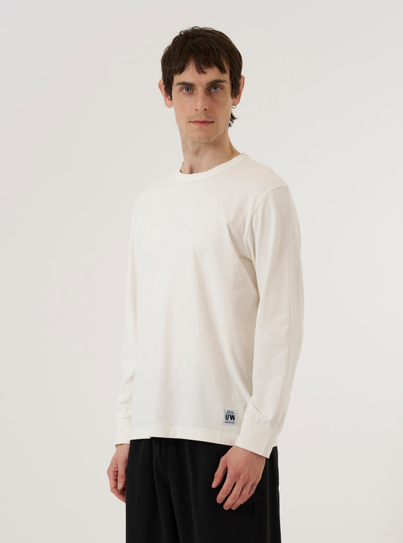 A model wears the Antique White Recycled/Bio Jersey Henry L/S Tee against a plain white background. The long-sleeved top features a three-button front placket at the neckline and is made from a smooth, off-white jersey fabric. The model is shown from the front, highlighting the garment's relaxed fit and clean construction.