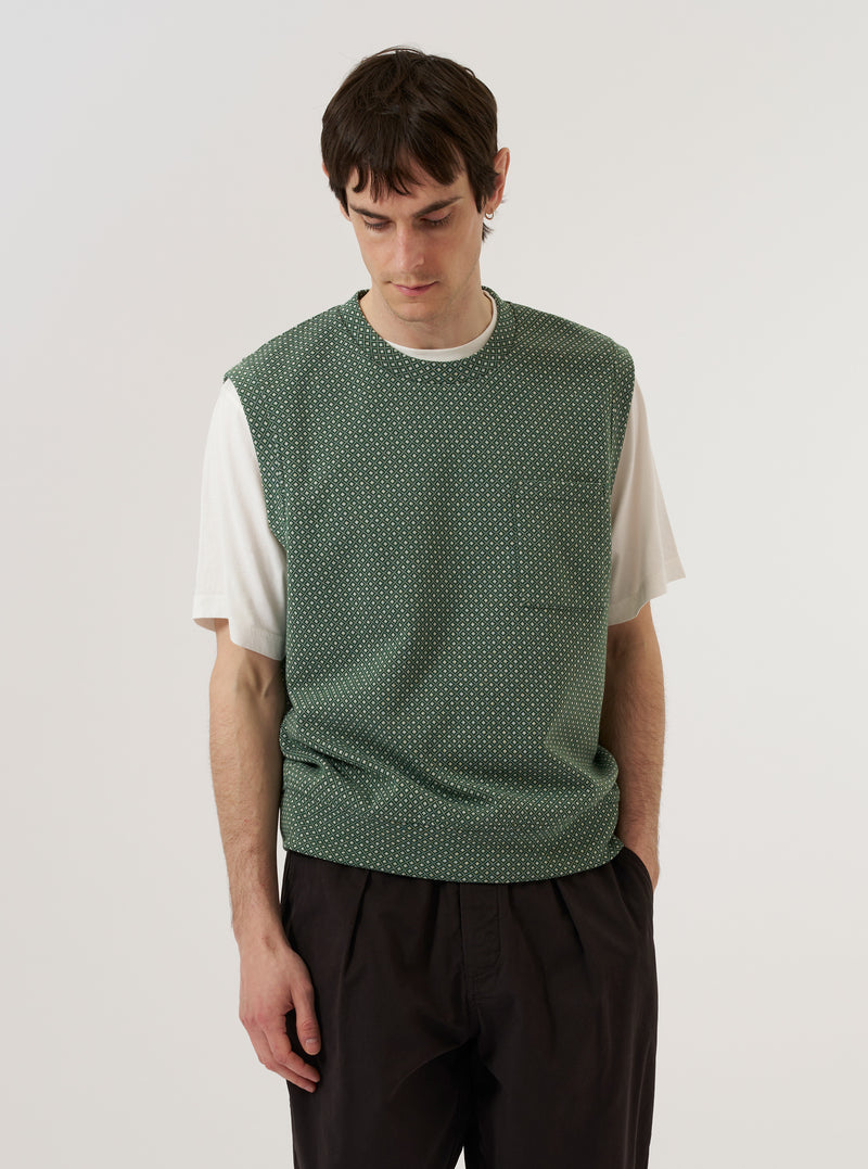A model wears the Green Argyll Jersey Sleeveless Crew against a plain, light-colored background. The sleeveless sweater features a bold green and white argyle diamond pattern with a ribbed crew neck and ribbed armholes. The model is shown from the chest up, layering the knit vest over a white collared shirt.