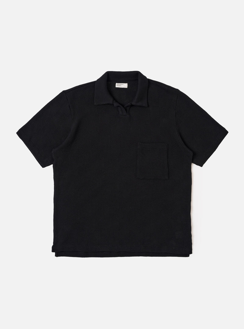 The Black Fantasy Checkerboard Vacation Polo is shown as a flat lay against a white background. The polo features an all-over black and grey checkerboard pattern, a one-piece open collar, a short buttonless placket, and a single patch pocket on the left chest. The short-sleeve garment has a stepped hem with side vents.