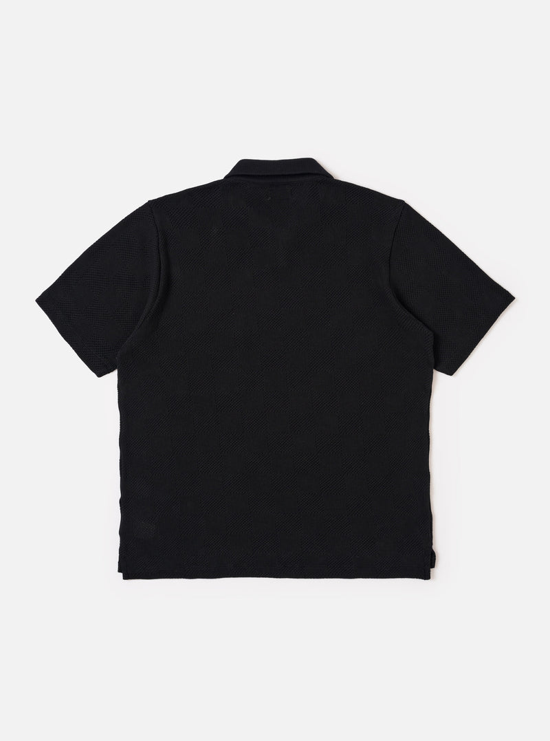 The Black Fantasy Checkerboard Vacation Polo is shown from the back as a flat lay against a plain white background. The image highlights the all-over black and grey checkerboard pattern, the structured one-piece collar, and a straight hem with small side vents.