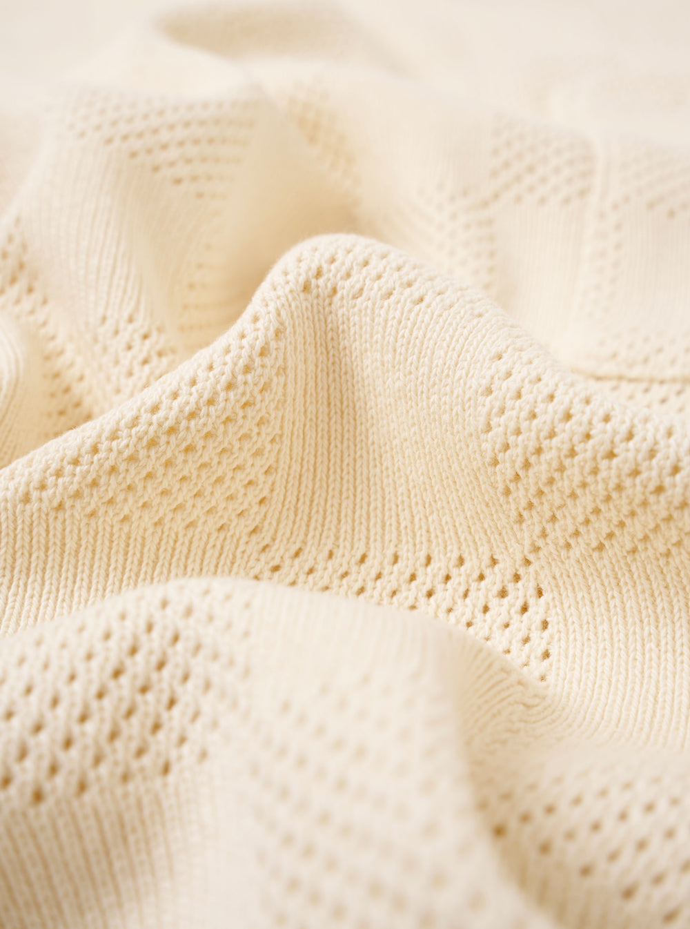 A close-up swatch of the Ecru Fantasy Checkerboard Vacation Polo highlights the intricate checkerboard knit pattern and the soft texture of the organic cotton fabric. The design features alternating shades of ecru and white, providing a detailed view of the garment's construction and material.