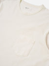 The Antique White Recycled/Bio Jersey Core Pocket Tee is shown from a rear angle as a flat lay against a plain white background. The image highlights the clean, simple construction of the t-shirt, featuring a ribbed crew neckline and a straight hem. The fabric is a solid antique white jersey with a smooth texture.
