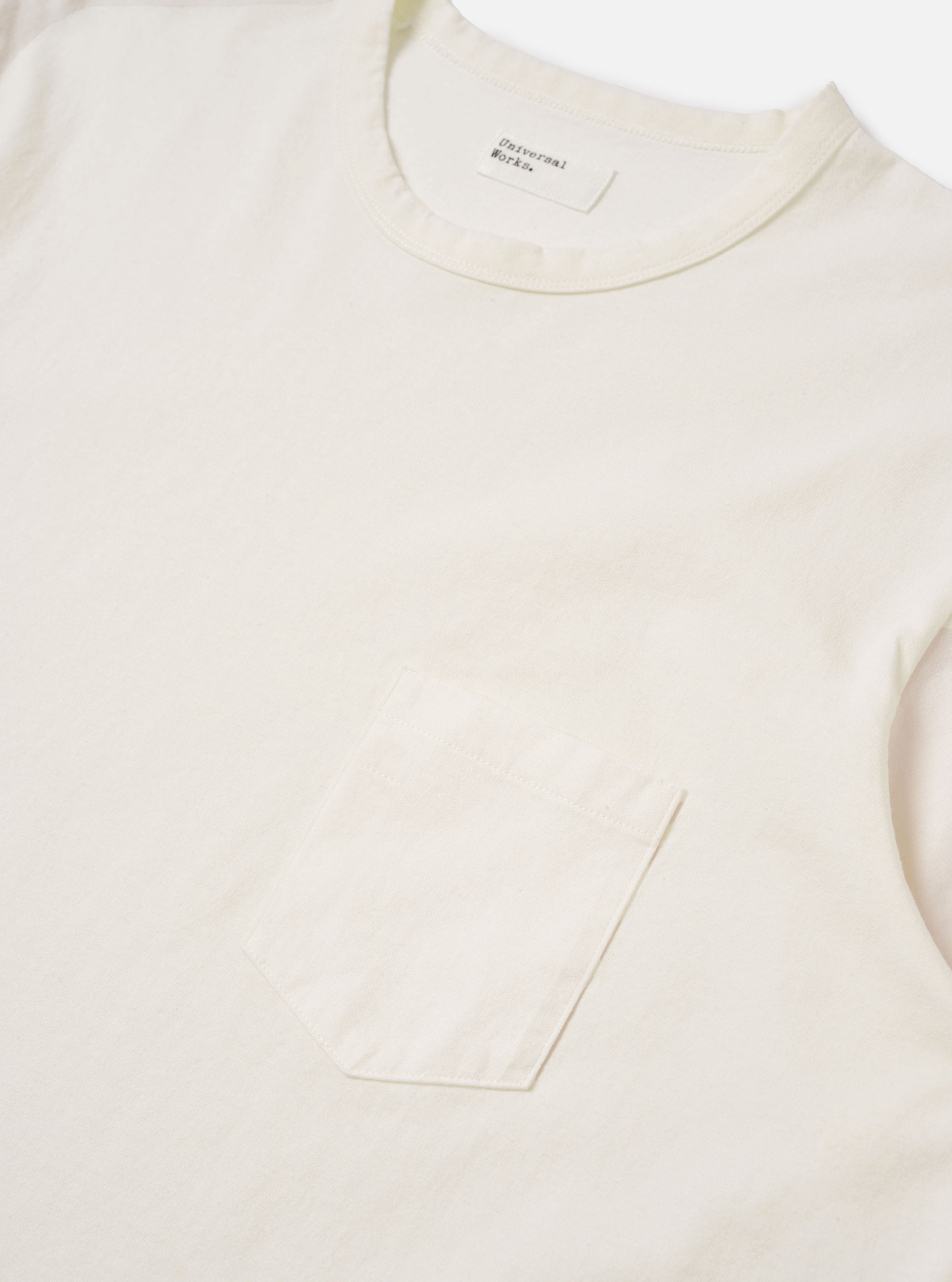 The Antique White Recycled/Bio Jersey Core Pocket Tee is shown from a rear angle as a flat lay against a plain white background. The image highlights the clean, simple construction of the t-shirt, featuring a ribbed crew neckline and a straight hem. The fabric is a solid antique white jersey with a smooth texture.
