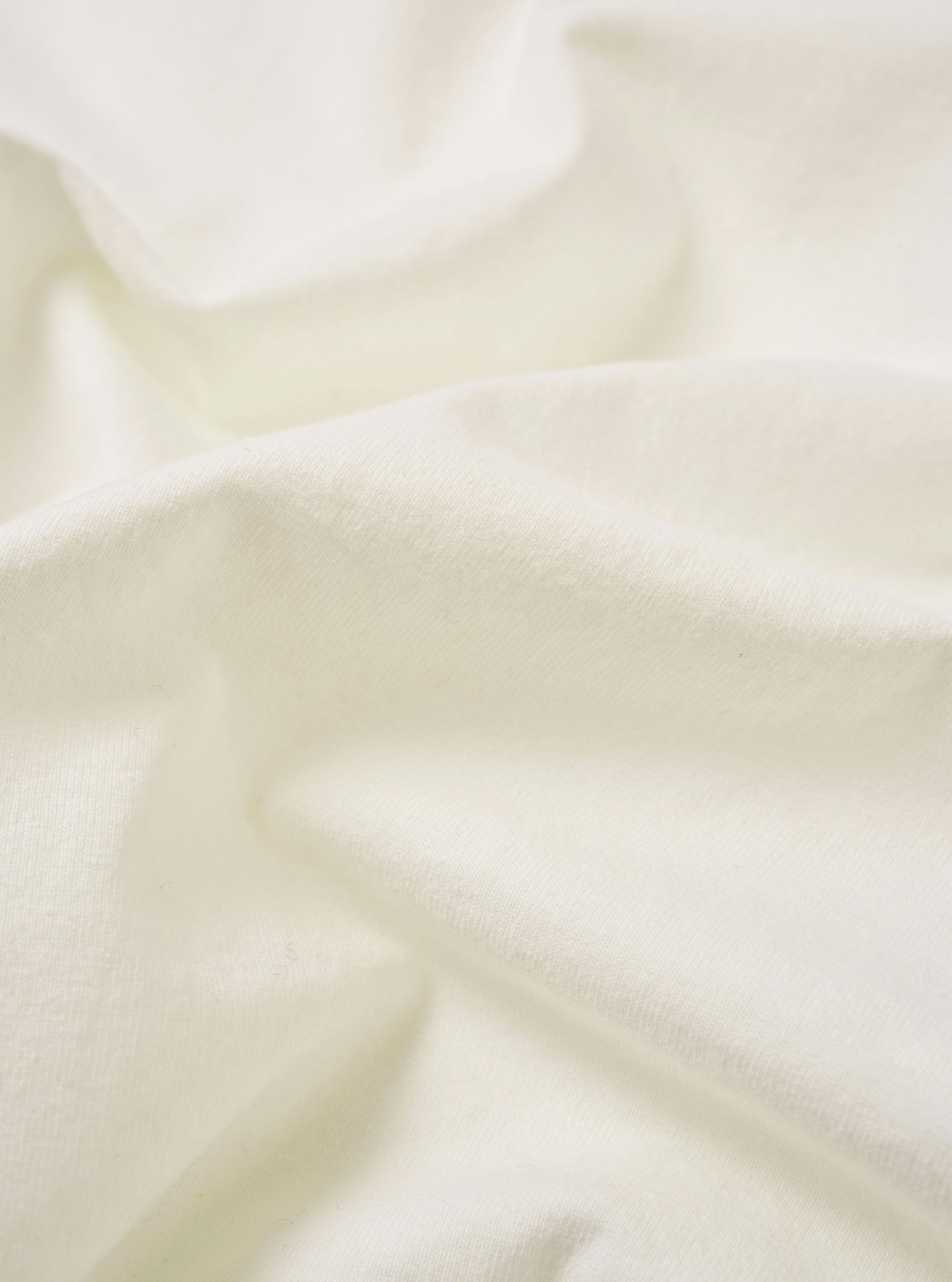 The Antique White Recycled/Bio Jersey Core Pocket Tee is shown in a detail view as a flat lay against a plain white background. The image highlights the textured antique white jersey fabric, the ribbed crew neckline, and the stitching of the front chest pocket.