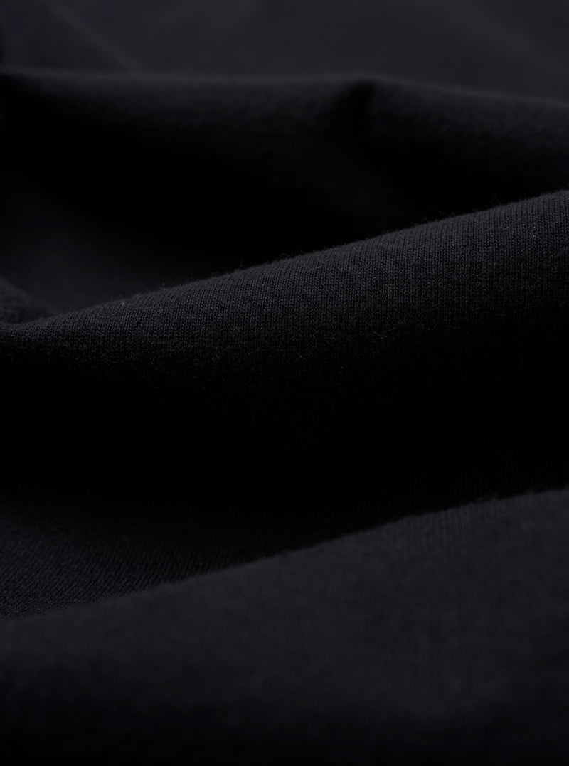A close-up swatch image of the Black Recycled/Bio Jersey Core Pocket Tee fabric displays a solid black color with a soft, fine jersey knit texture. The fabric fills the entire frame, providing a detailed view of the material.