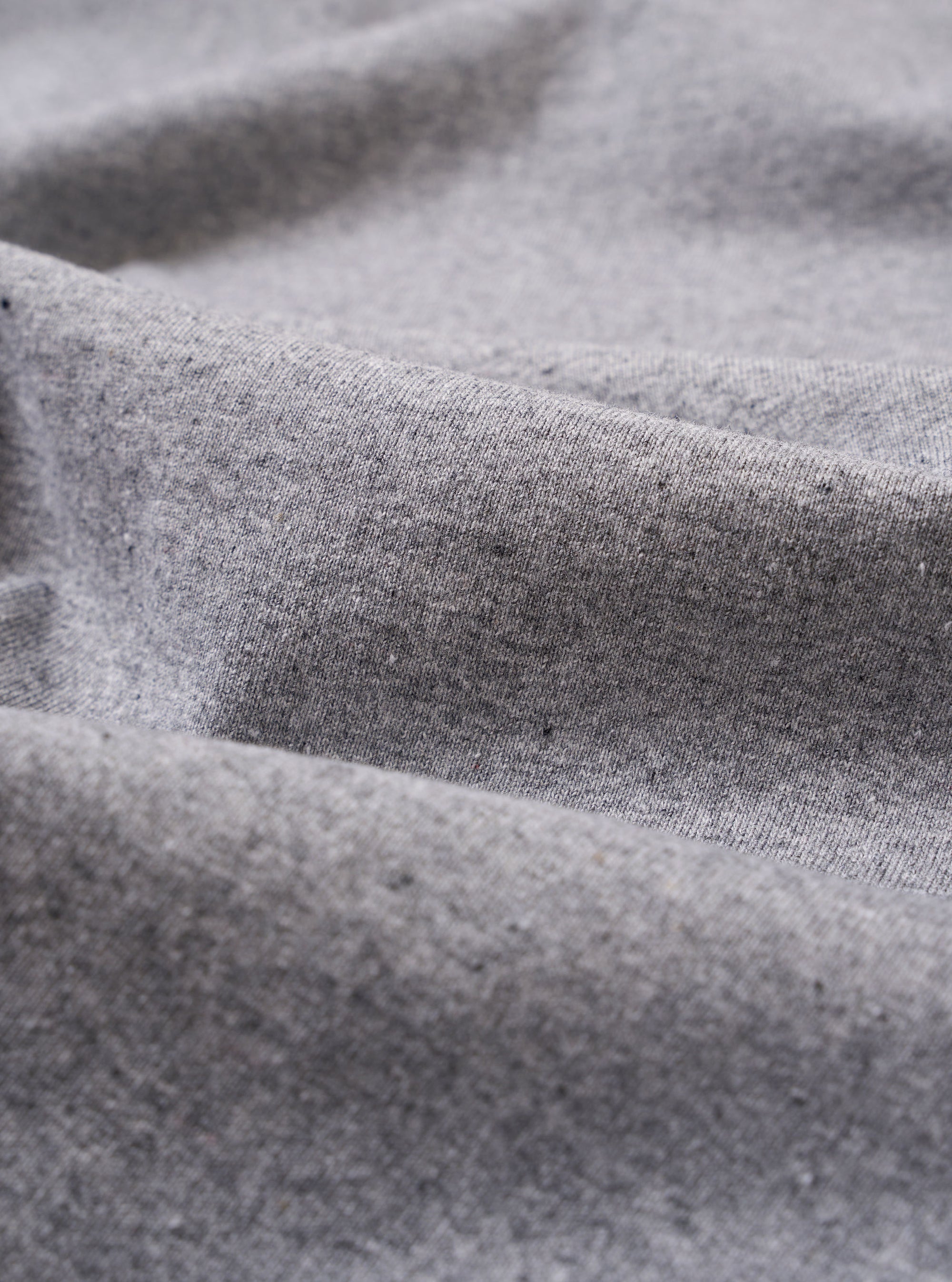 A close-up swatch image of the Grey Marl Recycled/Bio Jersey Core Pocket Tee fabric displays a light grey heathered texture with a soft, matte finish. The image focuses on the detailed knit of the recycled and organic cotton jersey material, filling the frame.