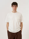 A model wears the Antique White Recycled/Bio Jersey Core Pocket Tee, standing against a plain white background. The T-shirt features a classic crew neck, short sleeves, and a single patch pocket on the left chest. The garment is made from a solid antique white jersey fabric with a smooth finish.