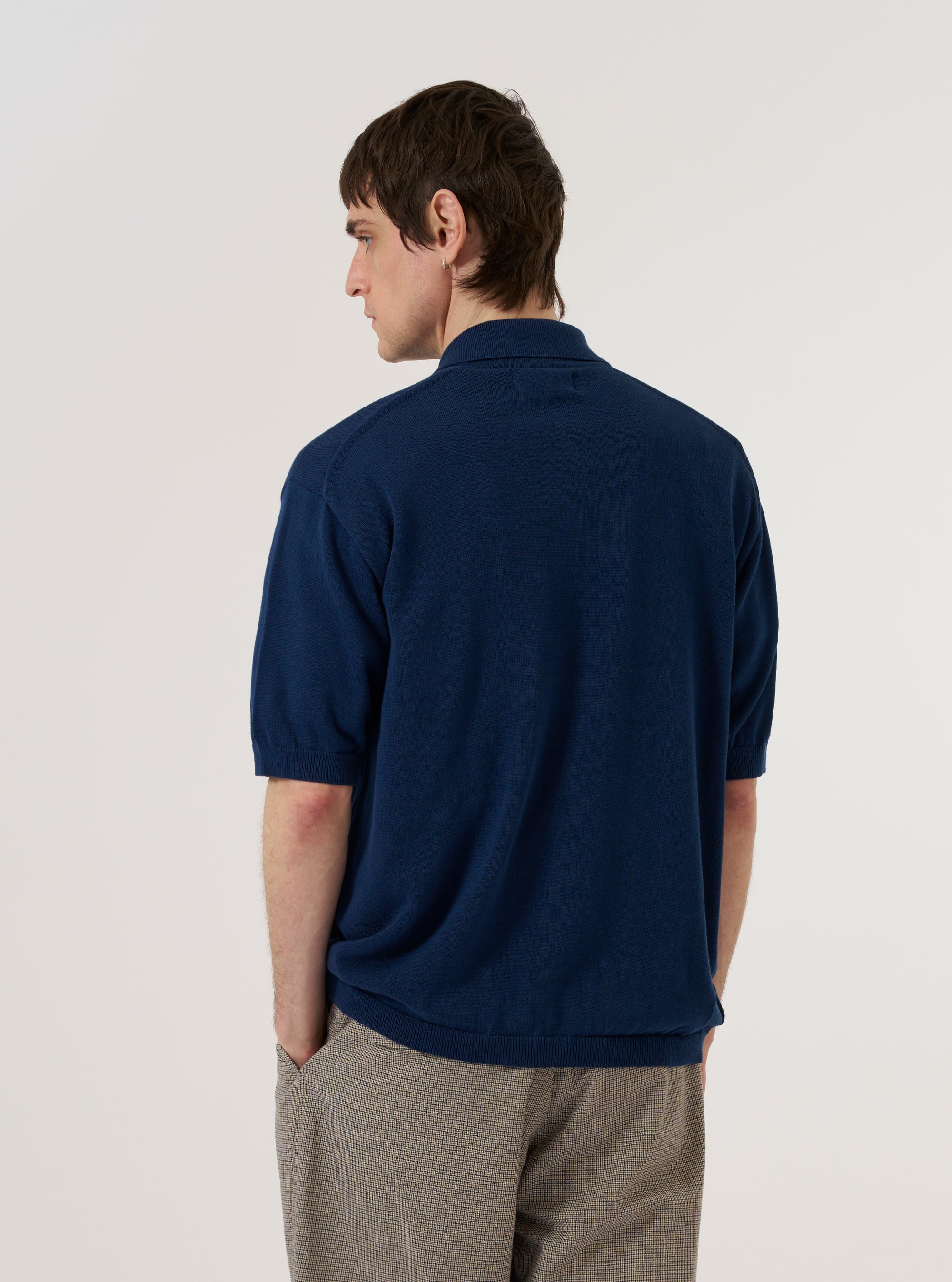 A model wears the Dark Navy Cotton Lace Knit Jonny Knit Shirt against a plain white background. The shirt features a distinctive open Jonny collar and an intricate, perforated lace-knit texture throughout the dark navy fabric. The model is shown from a rear three-quarter angle, highlighting the garment's construction and relaxed fit. No mannequin is present in the image.