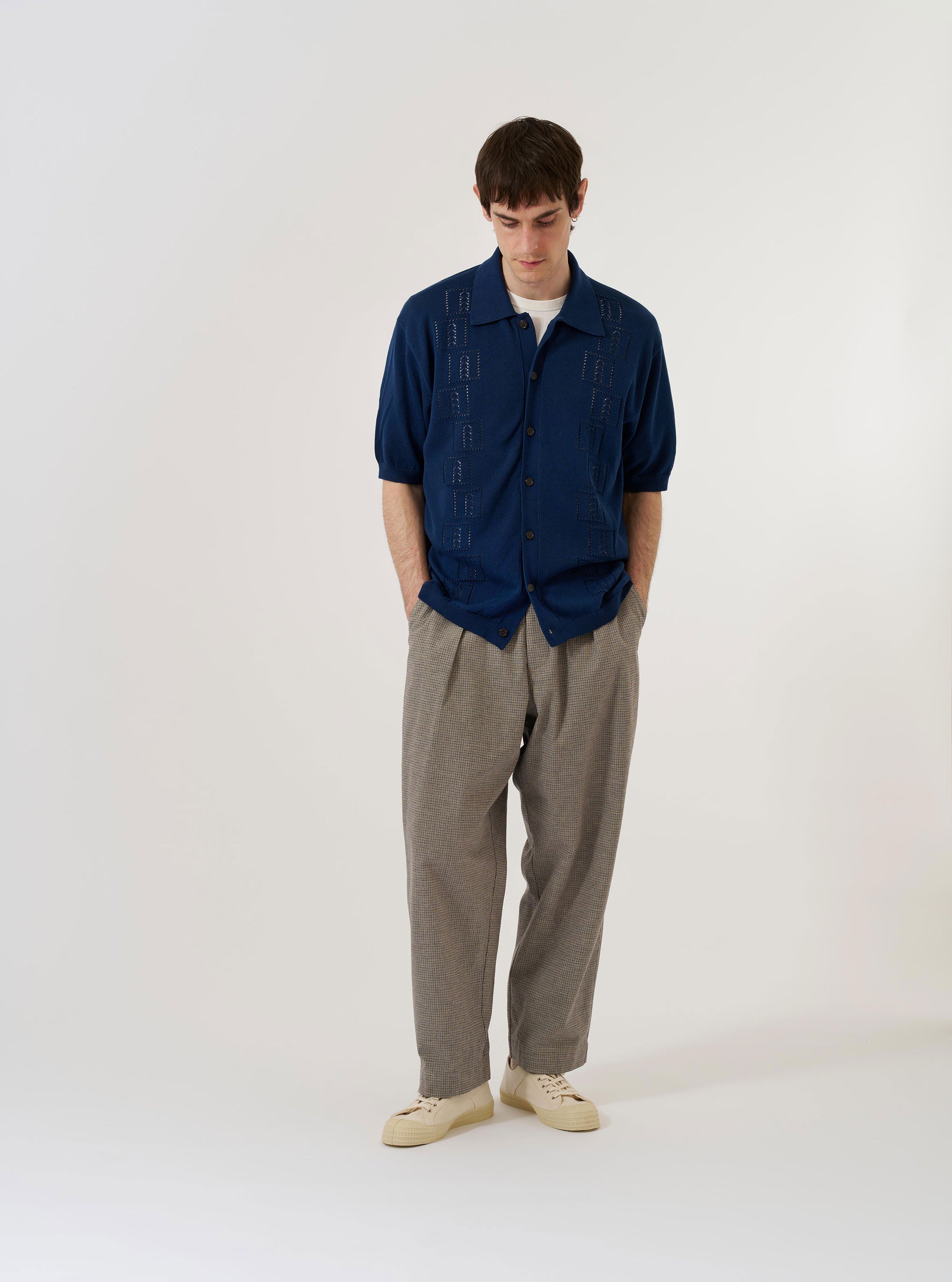 The Dark Navy Cotton Lace Knit Jonny Knit Shirt is presented as a flat lay against a plain white background. The shirt features an intricate lace-like knit texture, a wide open Jonny collar, and short sleeves. The design includes a ribbed hem and sleeve cuffs, emphasizing the dark navy cotton fabric.