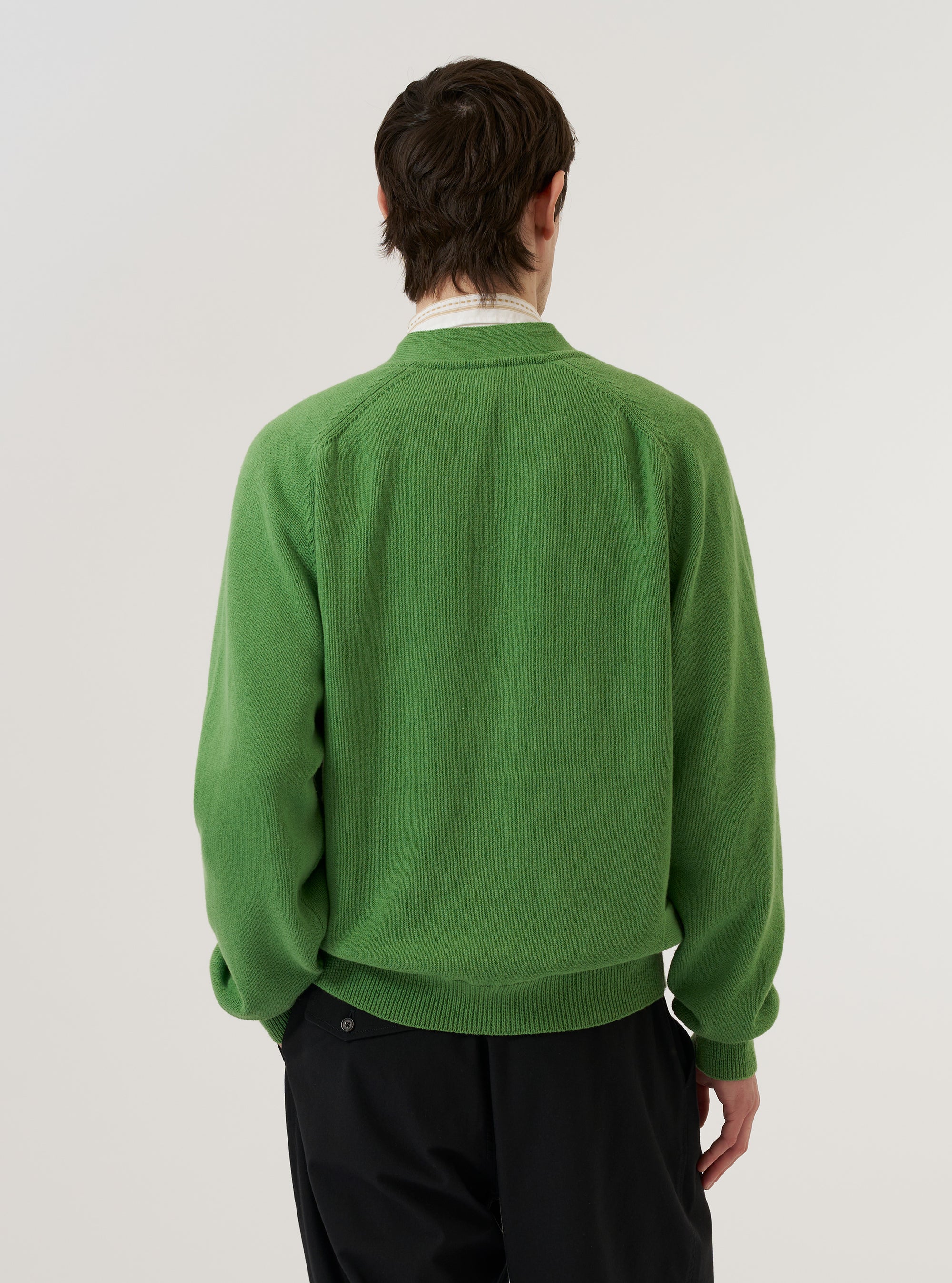 A model wears the Green Eco Cotton Knit Pocket David Cardigan over a light-colored shirt, shown from a side-angle view against a plain white background. The cardigan features a V-neckline, a button-down front, and a prominent patch pocket visible on the side. The olive green recycled cotton fabric displays a distinct knitted texture.