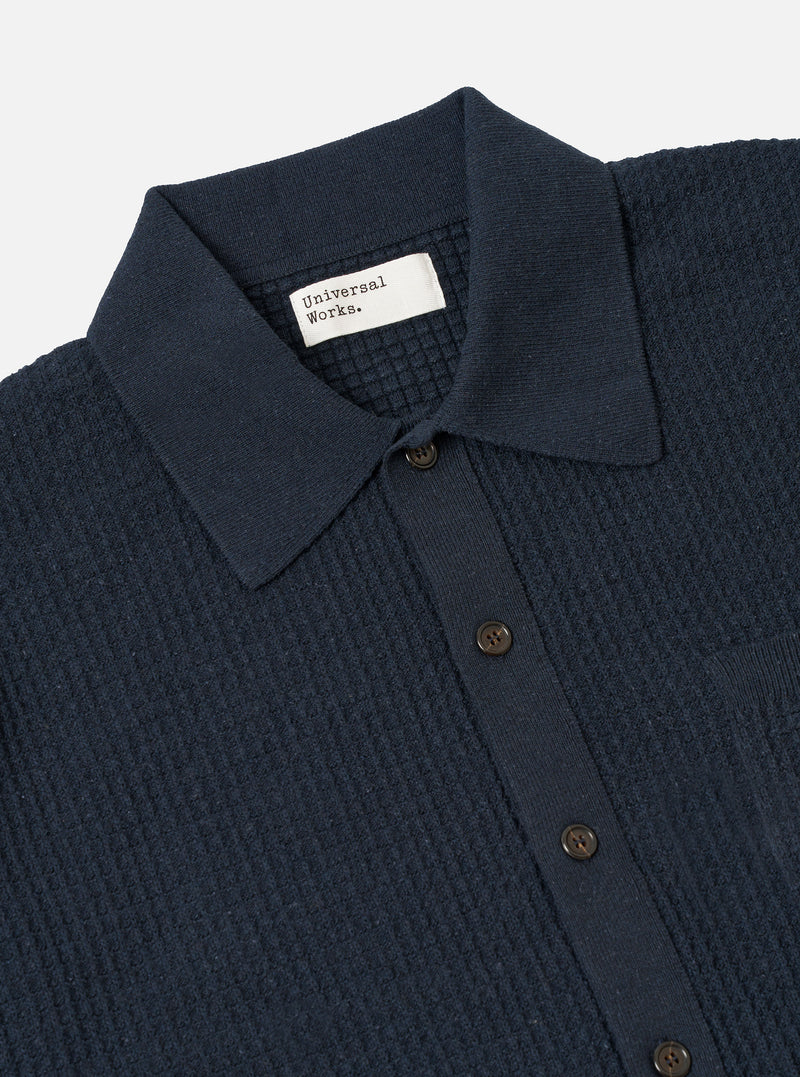 A model wears the Navy Eco Cotton Knit Jacket against a plain, light-grey background. The jacket features a five-button front closure, a structured collar, and two large patch pockets at the waist. The recycled cotton fabric has a visible, fine-gauge knitted texture.