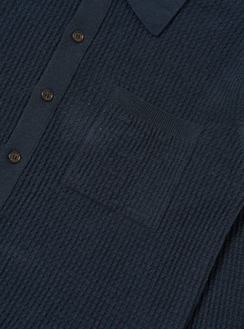 A close-up fabric swatch of the Navy Eco Cotton Knit Jacket highlights the detailed texture of the recycled cotton knit. The deep navy blue yarn is woven into a visible, structured pattern that creates a slightly raised surface.
