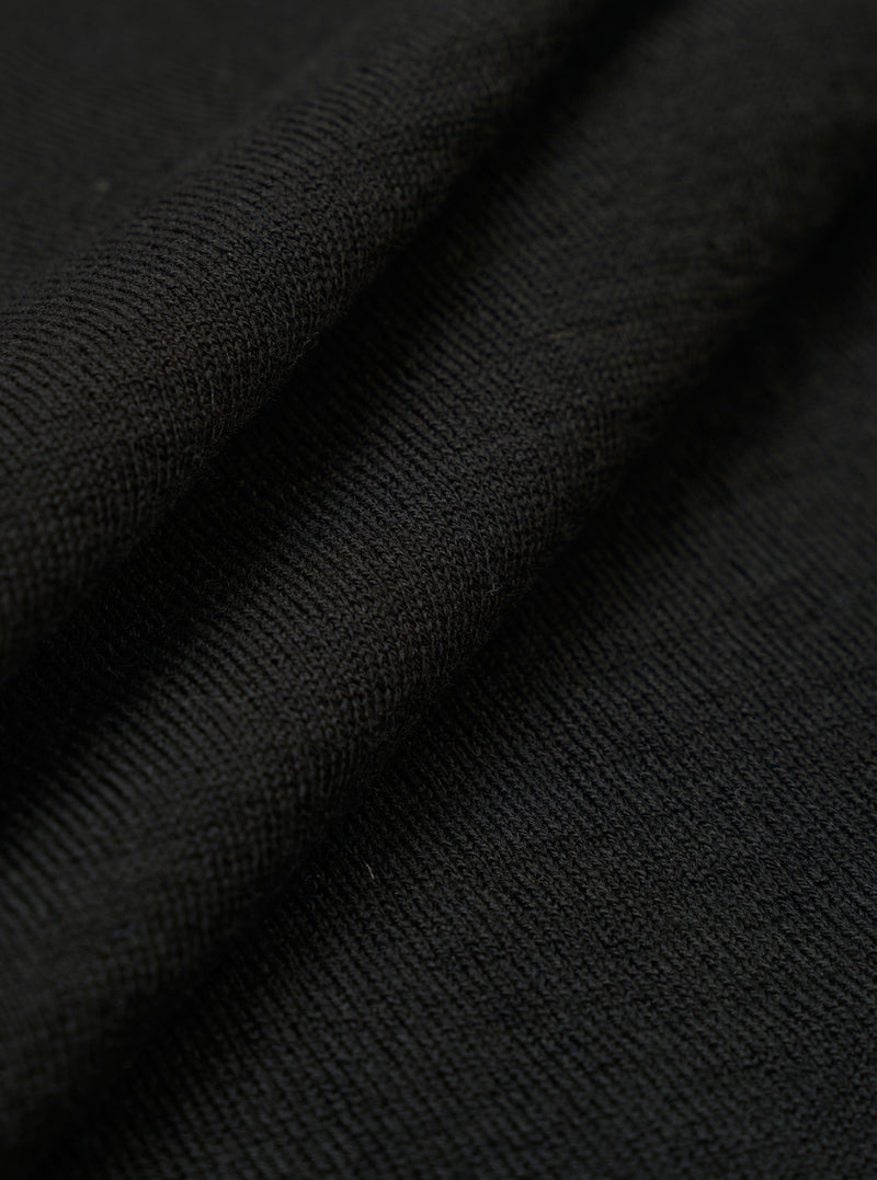 A close-up swatch of the Black Woolcot Bio S/S Pullover Knit Shirt II fabric highlights the smooth, fine-gauge texture of the black knit material. The image focuses on the blend of merino wool and organic cotton, with the fabric filling the entire frame.