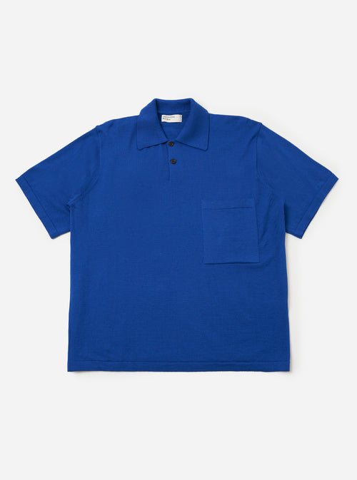 The Blue Woolcot Bio S/S Pullover Knit Shirt II is shown as a flat lay against a white background. The shirt features a boxy fit, short sleeves, a button placket, and a single chest pocket on the left side. The fabric is a smooth, solid blue knit.