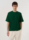 The Green Merino Fine Knit Knit Tee is worn by a model standing against a plain white background. The model is shown from the waist up, wearing the short-sleeved t-shirt which features a ribbed crew neckline and a fine-gauge knit texture. The garment has a relaxed fit and a clean, minimalist design.