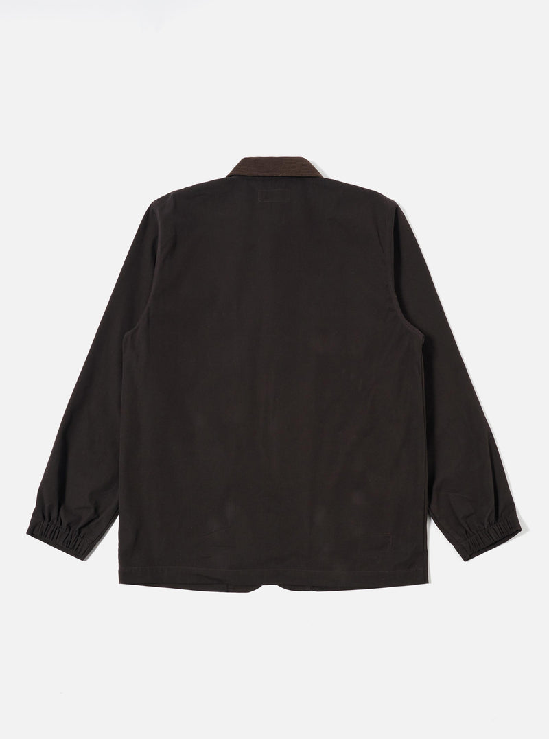 A model wears the Licorice Summer Canvas Labour Jacket against a plain, light-colored background. The jacket features four front patch pockets, with two chest pockets and two lower pockets that include buttoning flaps. The garment is shown in a loose, wide fit with a five-button front closure and a traditional collar. The fabric is a cotton canvas with a textured, matte finish.